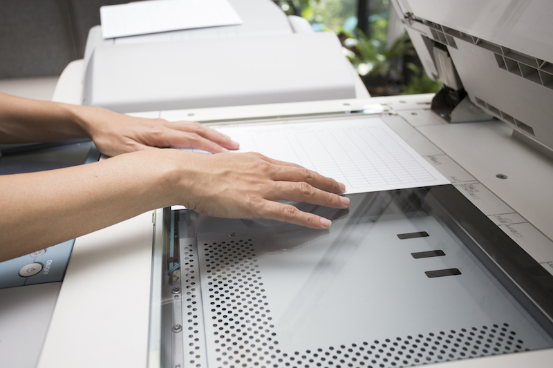 woman hands putting a sheet of paper into a copying device