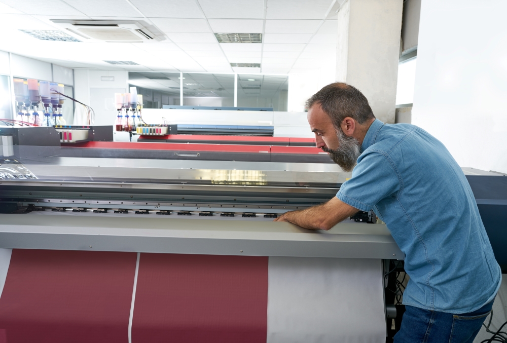 A man stands at a large printout on a wide format printer.