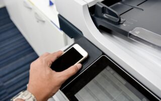 Copier security visualized with a person with their cell phone at a copier to verify their identity.