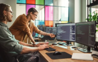 IT Services is represented by two young professionals standing over one of three screens in an office reviewing code.