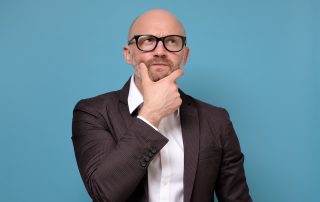 Professional man wearing glasses with hand on chin, blue background.