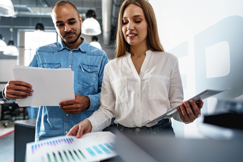 Two employees using new modern printer in office. Concept of secure printing, releasing prints at the printer.
